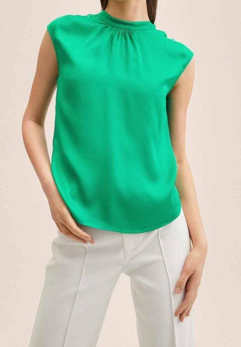 Haut sans manches vert avec un col froncé, en tissu lisse, associé à un pantalon blanc. Coupe simple et arrondie à l'ourlet.