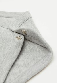 Světle šedá bavlněná látka složená na límci, s kovovými cvoky a texturovaným povrchem podél okrajů.