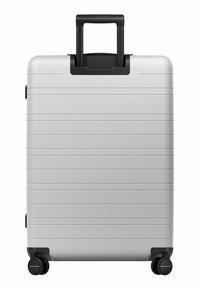 Valise rigide argentée avec une surface texturée, poignée et roues noires, présentant des rayures horizontales pour une meilleure adhérence et un style accru.