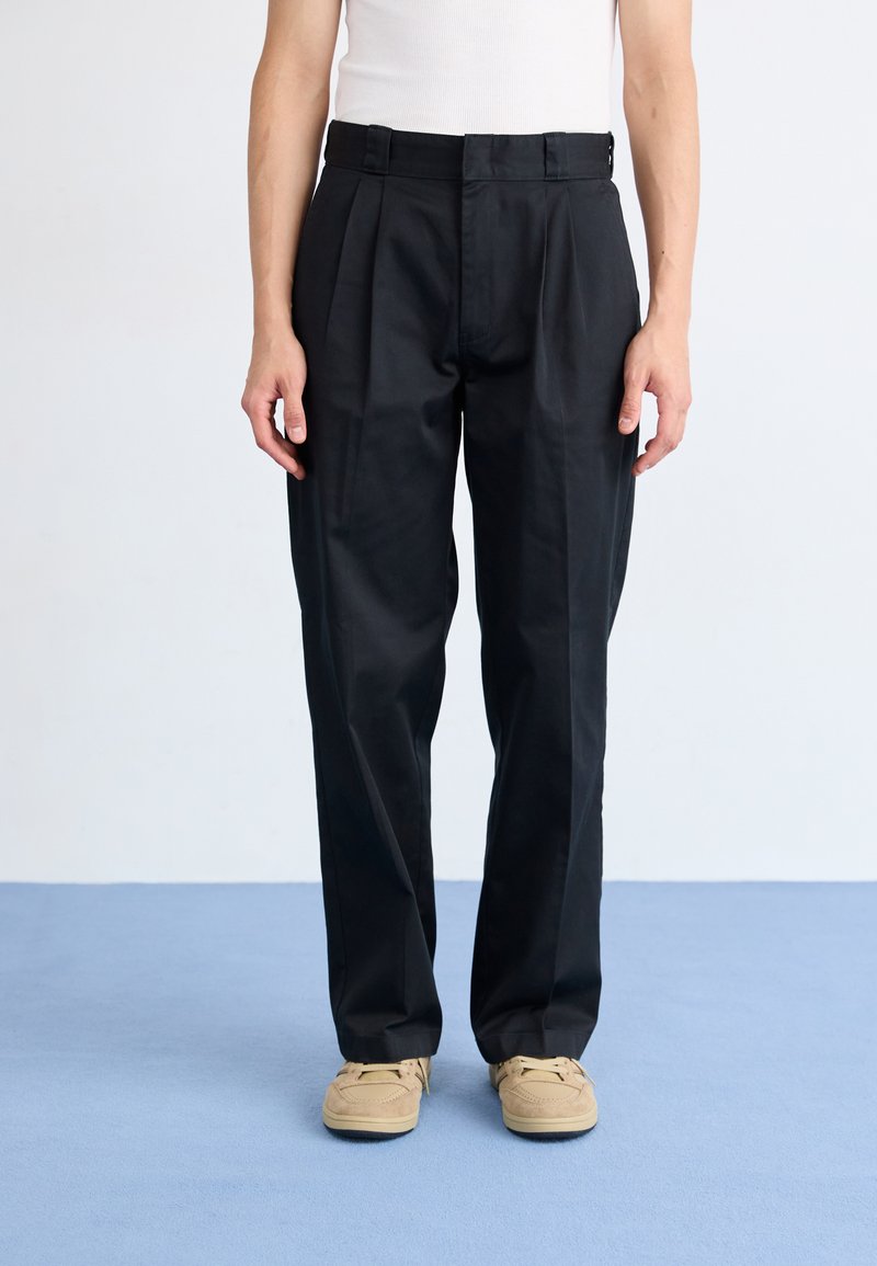 Pantaloni neri plissettati con una vestibilità rilassata, caratterizzati da una vita alta e tasche laterali. Realizzati in un tessuto liscio, impreziositi da dettagli minimi.