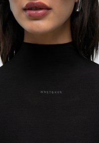 Černý žebrovaný rolák s jemným logem "WRSTBHVR" potisknutým šedou barvou v oblasti hrudníku. Hladká textura, přiléhavý střih.