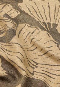 Tekstilstof med en tekstureret satinoverflade og gyldne og mørke mønstre, der ligner bladdesign, hvilket skaber et rigt, lagdelt udseende.