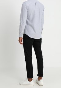 Ljusblå långärmad skjorta med knappkrage, detalj med veck bak och rundad nederkant; matchad med svarta uppvikta byxor och vita sneakers.