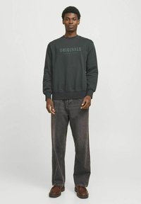 Donkergrijze sweatshirt met de tekst "ORIGINALS" gecentreerd op de borst, gecombineerd met een losse, donkere denim jeans en bruine schoenen.