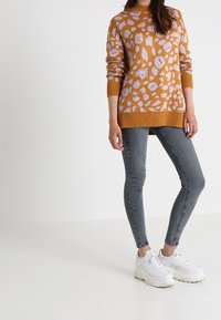 Senapsgul tröja med ljuslila leopardmönster, ribbade ärmslut och nederkant. Buren med ljusgrå skinny jeans och vita sneakers.