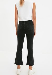 Svarta utsvängda jeans med hög midja, med bakfickor och fransiga fållar, kombinerade med en vit stickad ärmlös topp.