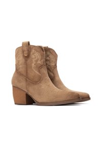 Botines de ante color marrón claro con costuras decorativas, puntera puntiaguda y tacón apilado. Presentan lengüetas para facilitar su uso.