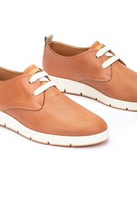 Zapatillas de cuero marrón con cordones blancos, que presentan una textura perforada y una suela blanca acolchada para mayor comodidad y soporte.