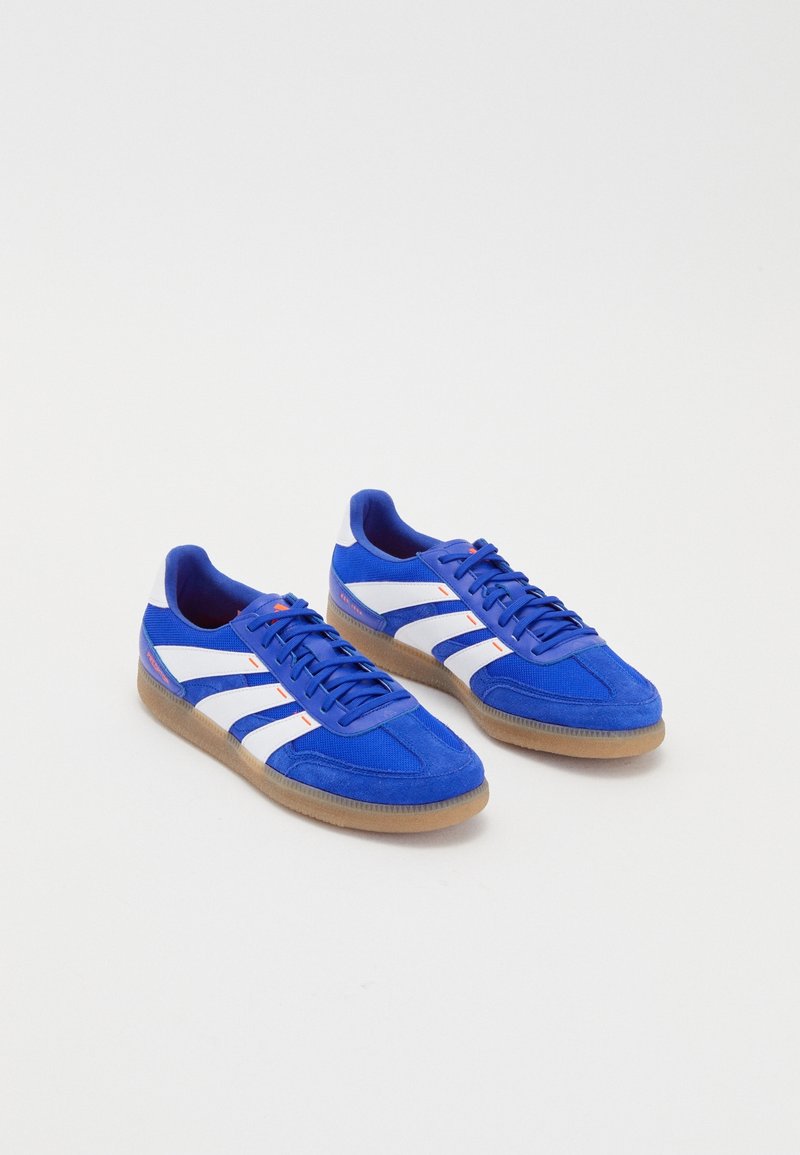 Par de zapatillas azules con rayas blancas, suelas de goma y cordones azules sobre un fondo blanco liso.