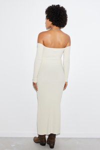 Robe longue à épaule dénudée en crème, avec des manches longues et une silhouette ajustée. Portée avec des bottines brunes.