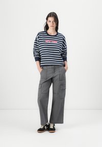 Marineblå og hvitstripet sweatshirt med "NEW YORK" i rødt sentrert på brystet, parret med løse grå cargo-bukser og sorte sneakers.
