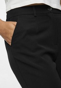 Schwarze maßgeschneiderte Hose aus gewebtem Stoff mit glatter Textur, seitlichen Taschen und einem Knopfverschluss in der Taille.