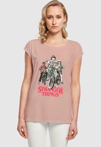 Hea roosa puuvillane t-särk, millel on "Stranger Things" graafika neljast tegelasest jalgratastel. Lühikesed varrukad ja vabalt lõigatud.