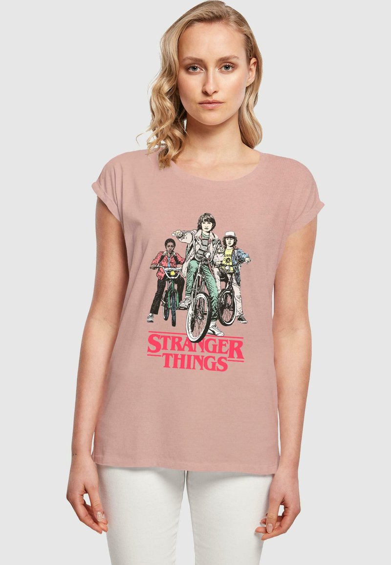 Hea roosa puuvillane t-särk, millel on "Stranger Things" graafika neljast tegelasest jalgratastel. Lühikesed varrukad ja vabalt lõigatud.