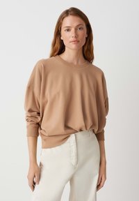 Felpa beige morbida e comoda con scollatura tonda e spalle scese, abbinata a pantaloni crema chiari. Tessuto liscio, senza motivi visibili.
