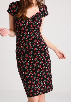 Femme portant une robe noire longueur genou avec un motif de cerises rouges et de feuilles vertes, manches courtes et taille cintrée.