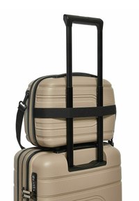 Beige harde koffer met een gestructureerde afwerking. Uittrekbare handgreep en zwarte riem die een kleinere tas bovenop beveiligt. Combinatieslot zichtbaar.