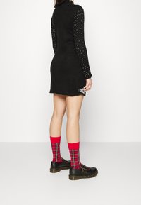 Svart stickad klänning med långa ärmar som har vita prickar, i kombination med röda rutiga strumpor och svarta skor med spänne.