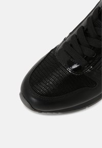 Baskets noires avec une tige brillante et texturée arborant un motif en grille, fermeture à lacets et semelle en caoutchouc solide. Accents en cuir lisse présents.