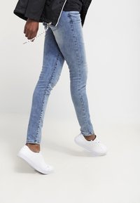 Vaaleansiniset slim fit -farkut, valmistettu denimistä, yhdistettynä valkoisiin kangaskenkäisiin, joissa on pyöreä kärki ja litteät pohjat.