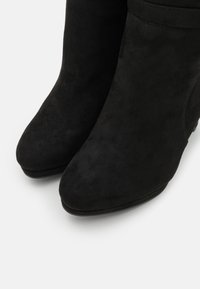 Botas de tobillo de ante negro con punta afilada y tacón bajo de cuña, que presentan una textura suave y líneas limpias.