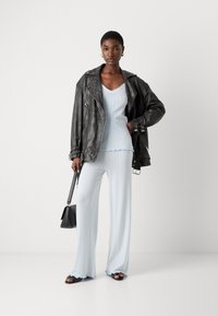 Hellblaues gestricktes Oberteil und Hose im Set mit texturiertem Rippmuster. Schwarze Lederjacke im Oversized-Stil mit silbernen Beschlägen und ausgefransten Hosenumschlägen. Schwarze Accessoires.