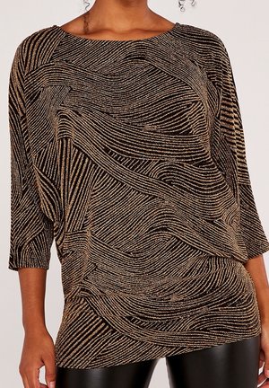Haut à manches longues rayé noir et or avec un motif abstrait en spirale, porté avec un pantalon en cuir synthétique noir.