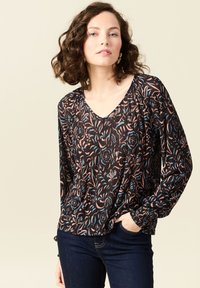 Blusa nera a maniche lunghe con motivo floreale in rosa e blu. Design a V con costine testurizzate. Abbinata a jeans scuri.