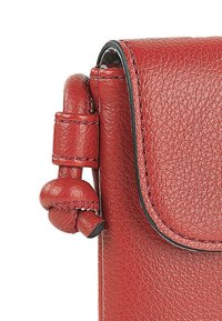 Bolso de cuero rojo con acabado texturizado, que presenta un cierre de solapa magnético y un acento de cuero anudado en el lateral, destacando los detalles de la artesanía.