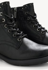 Botas de tobillo de cuero negro con cordones en la parte delantera, cierre de cremallera y acentos metálicos cerca del collar y los ojetes. Suela texturizada sólida.