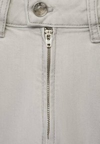 Grå denimtyg har en central metalldragkedja med en YKK-tab, kompletterad av en metallknapp och förstärkt sömnad vid midjan.