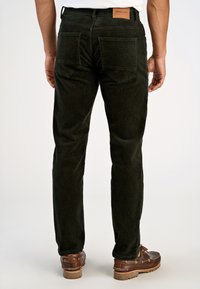 Pantaloni in corduroy verde scuro con vestibilità a gamba dritta e due tasche posteriori. Etichetta in pelle sulla vita. Indossati con scarpe stringate marroni.