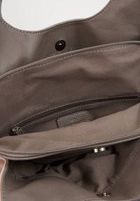 Grijze leren handtasinterieur met een gladde textuur, een ritsvak en een merketiket. De voering is van een bijpassende grijze stof.