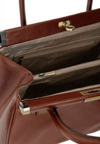 Brązowa skórzana torebka o teksturowanym wykończeniu, złotym sprzęcie i beżowym wnętrzu z materiału, zawierająca kieszenie na zamek i kieszenie wsuwane.