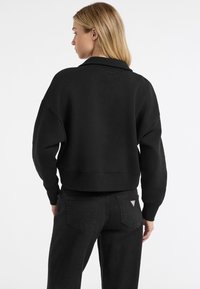 Czarny krótki sweatshirt o luźnym kroju, z opadającymi ramionami i ściągaczami. W zestawie z czarnymi spodniami o prostych nogawkach z tylnymi kieszeniami.
