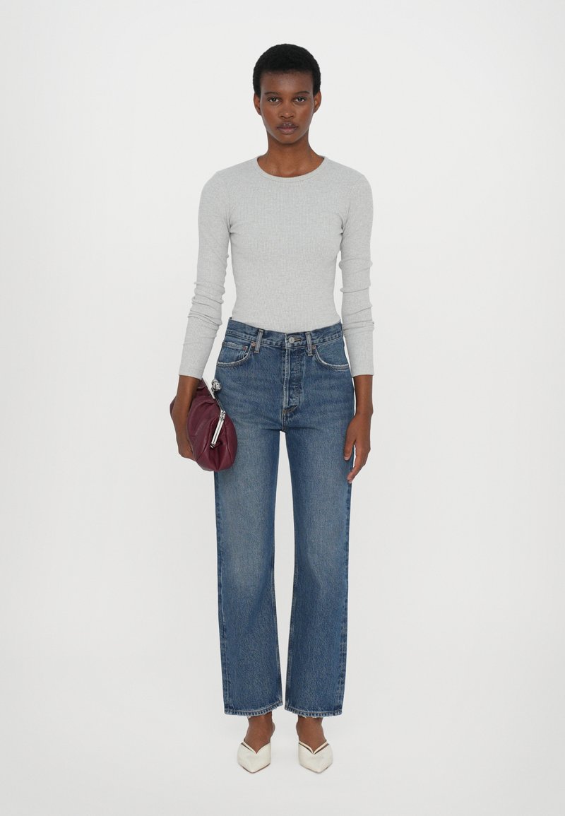 Light gray long-sleeve ribbed top, high-waisted blue denim wide-leg jeans, white pointed-toe shoes, holding a burgundy handbag.