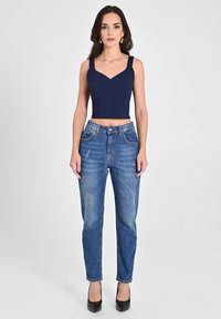 Top corto blu navy con spalline larghe, abbinato a jeans in denim blu a vita media con leggera usura e taglio dritto, completato da tacchi neri.