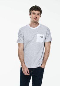 Šedé pruhované tričko s krátkým rukávem, kulatým výstřihem a kapsou na prsou. Tričko má bílý akcent na kapse a potištěný textový detail.