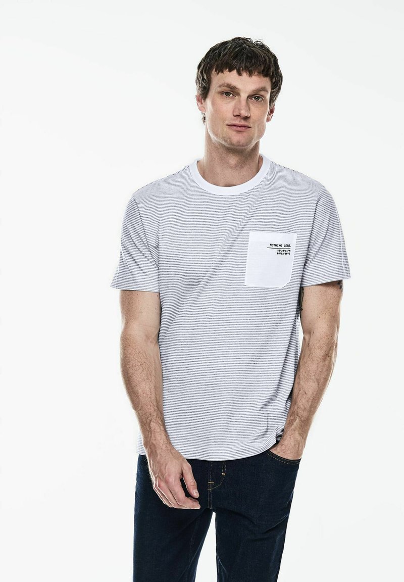 Šedé pruhované tričko s krátkým rukávem, kulatým výstřihem a kapsou na prsou. Tričko má bílý akcent na kapse a potištěný textový detail.
