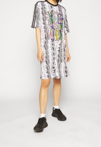 Harmaa ylisuuri t-paitamekko mustalla raidalla, jossa on monivärinen "LOVE UNITE" -painatus ja rento istuvuus. Mustat lenkkarit jalassa.