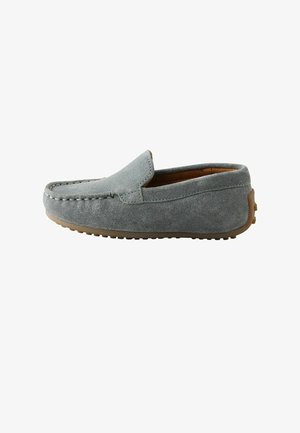 Pelēks zamšādas slip-on loafer apavu pāris ar brūnu gumijas zoli un šuvju detaļām gar augšējo malu, skatīts no sāniem.