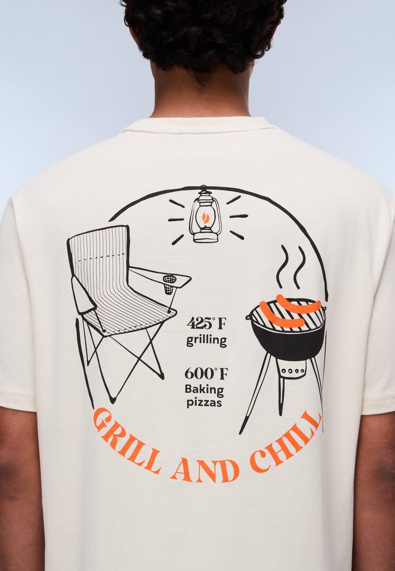 Weißes T-Shirt mit schwarzem und orangefarbenem Grafikdesign eines Stuhls, Grills, einer Laterne und dem Text "GRILL AND CHILL" mit Temperaturangaben.