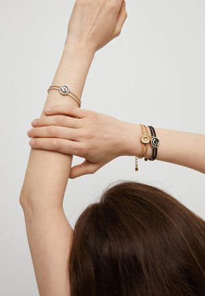 Cuatro pulseras de diferentes colores: una banda plateada con un detalle circular, una banda dorada y dos bandas de cuero en negro y marrón.