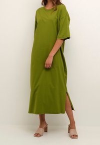 Grön bomulls-middress med korta ärmar, rund halsringning, sidokilar och en lös passform. Bärs med beigefärgade blockklackar.