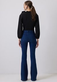 Top nero a maniche lunghe con un design aderente, abbinato a jeans blu a vita alta con gamba svasata. Il denim ha una superficie liscia; il tessuto elasticizzato garantisce comfort.