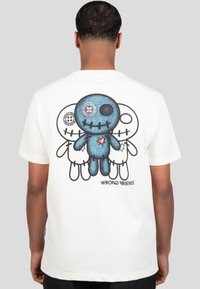 Camiseta de algodón blanca con un gráfico de un muñeco de felpa azul rodeado de dos figuras de contorno. El texto impreso en la parte inferior dice "AMIGOS INCORRECTOS."