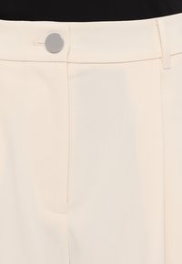 Cr�ème kleurige broek met een gladde textuur, voorzien van een voorzak, een zilveren knoopsluiting en een op maat gemaakte pasvorm.