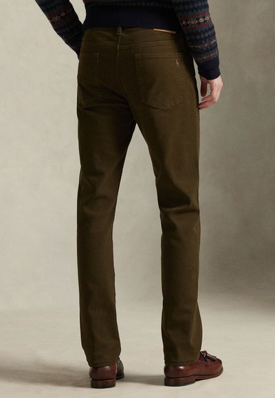 Olivengrønne bomullsbukser med rett ben-design. Har to baklommer og en liten logo nær linningen, brukt med brune sko.