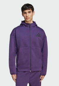Felpa con zip viola realizzata in tessuto morbido, dotata di una tasca frontale, dettagli in logo neri e cappuccio aderente.