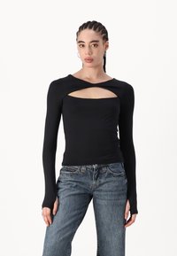 Black long-sleeve top with a twisted design and cut-out at the chest. Soft, stretchy fabric; paired with light wash denim jeans.